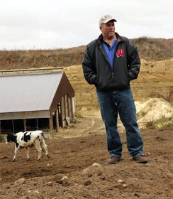 Wisconsin dairy farmer with barn and sand mine in background