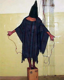 Abu Ghraib torture--hooded man hooked up to wires and standing on a box