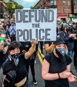 Marching protestor holding "Defund the Police" sign