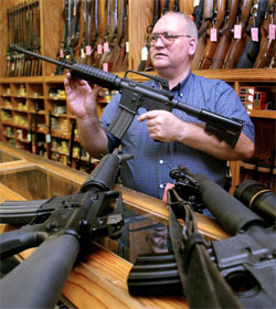 Man at gun shop counter surrounded by assault weapons